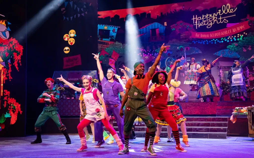 Happyville Heights pantomime ensemble performing on a colourful theatrical set under vivid stage lighting